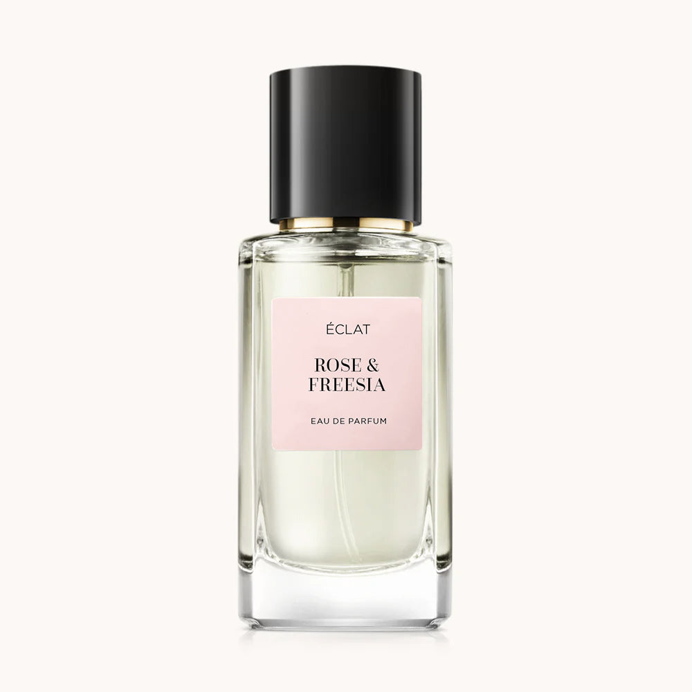Flacon of the women’s perfume dupe ÉCLAT Rose & Freesia, an elegant transparent glass bottle with a black cylindrical magnetic cap and a light pink label. The label displays the brand name ÉCLAT, the name Rose & Freesia, and the phrase “Eau de Parfum”.