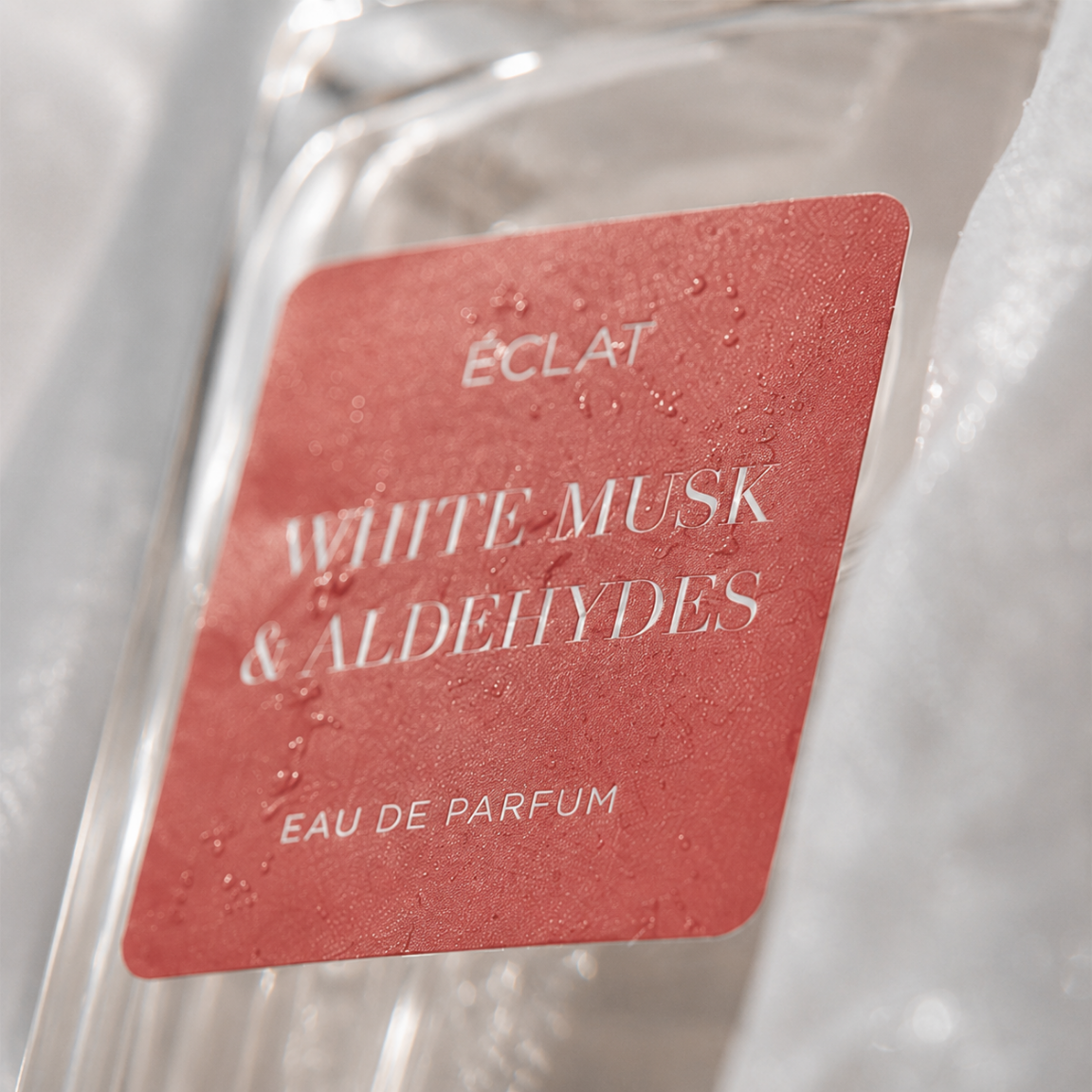 Nahaufnahme des ÉCLAT White Musk & Aldehydes Parfümflakons mit rotem, strukturiertem Etikett.