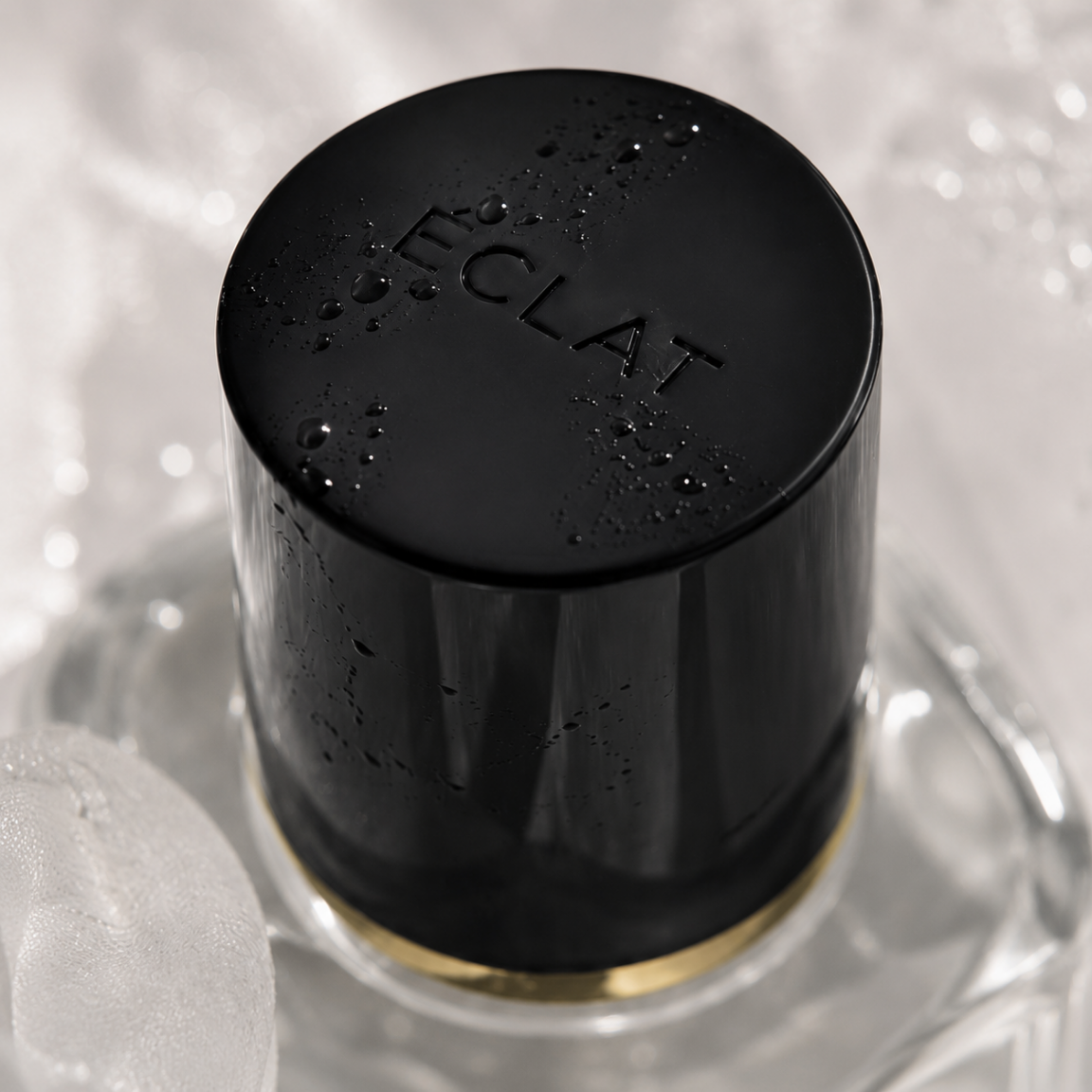 Facettierter Glasflakon mit schwarzem Verschluss, geprägt mit ÉCLAT, verziert mit Wassertropfen.