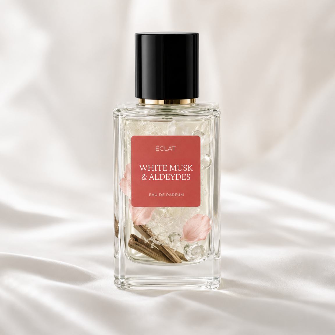 ÉCLAT White Musk & Aldehydes in einem facettierten Glasflakon mit schwarzer Kappe und rotem Etikett auf weichem, weißem Stoffhintergrund.