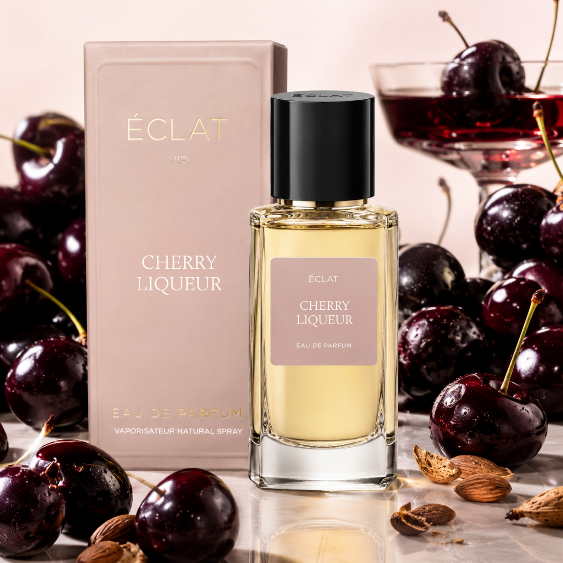 Das Bild zeigt das ÉCLAT Cherry Liqueur Parfum mit facettiertem Glasflakon und schwarzem Verschluss, neben einer rosa Schachtel und frischen Kirschen.