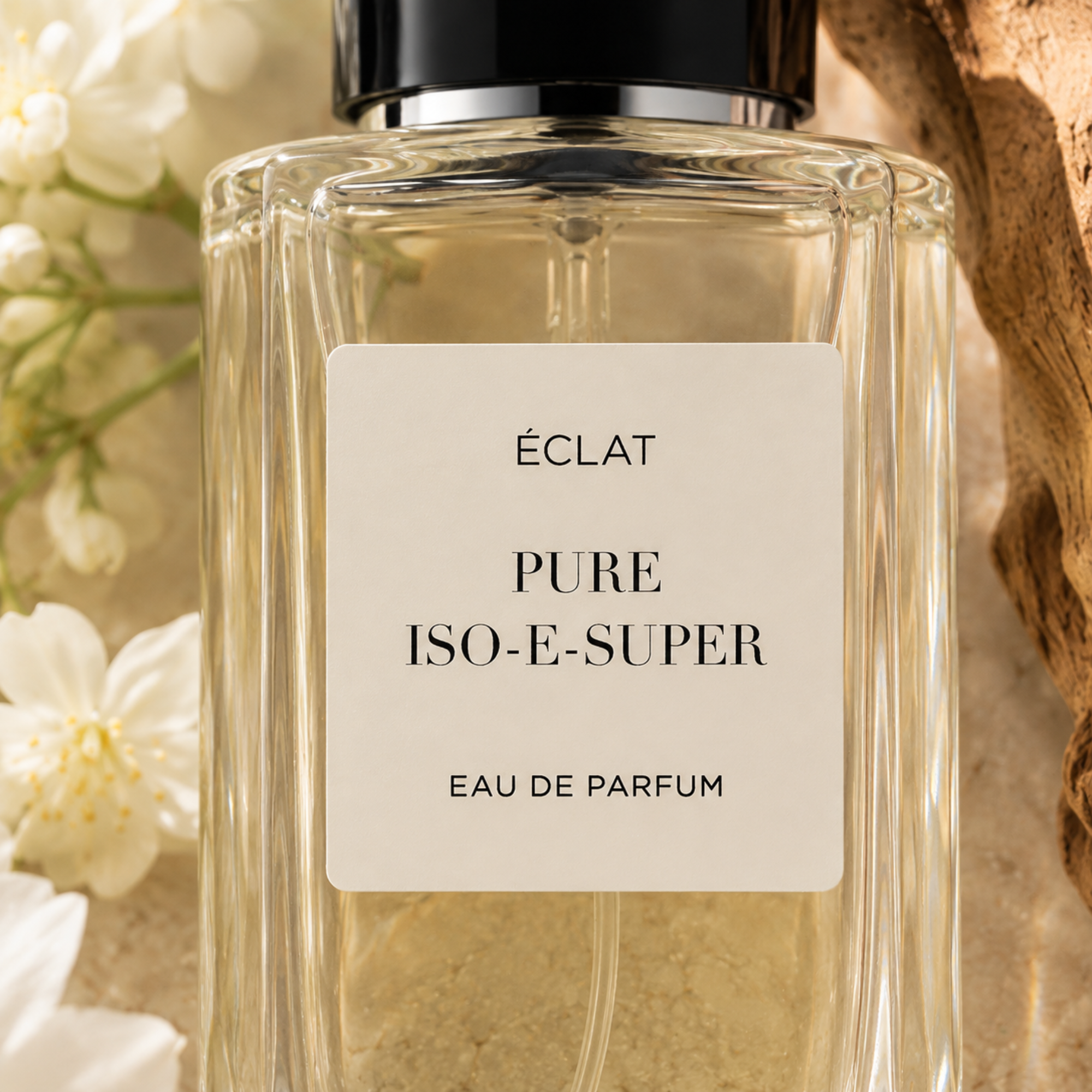 Ein facettierter Glasflakon von ÉCLAT Pure Iso-E-Super mit schwarzem Verschluss, umgeben von weißen Blüten und strukturiertem Holz.