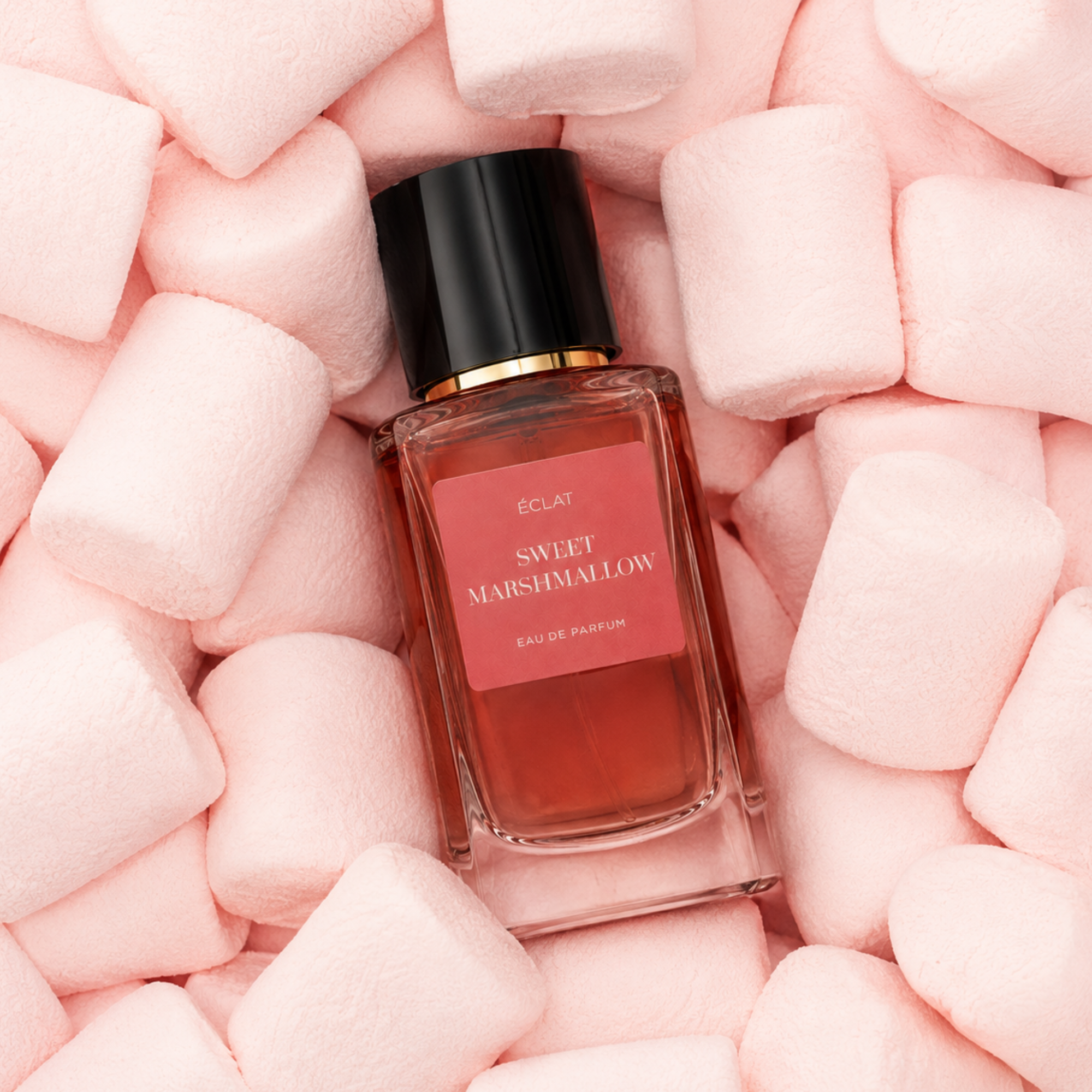 Ein Glasflakon von ÉCLAT Sweet Marshmallow, umgeben von weichen rosa Marshmallows, mit schwarzem Verschluss und rosa Etikett.