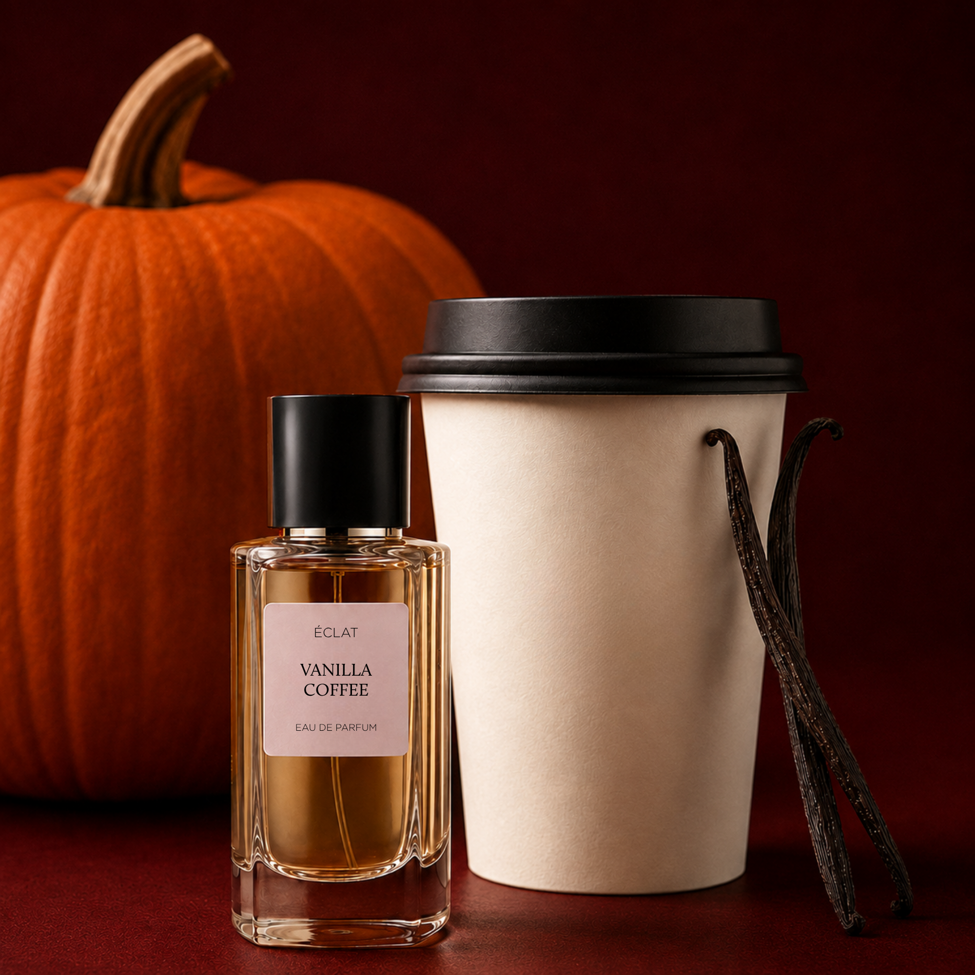 Ein facettierter Glasflakon von ÉCLAT Vanilla Coffee mit schwarzer Kappe steht neben einem Kaffeebecher und Vanilleschoten, mit einem Kürbis im Hintergrund.