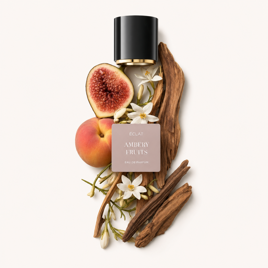 Ein Arrangement aus einer halbierten Feige, einem ganzen Pfirsich, weißen Blüten und Holzelementen umgibt das ÉCLAT Ambery Fruits Etikett unter einer schwarzen Kappe mit goldenem Inneren.