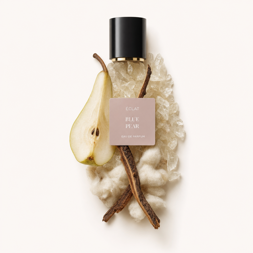 Ein elegantes Arrangement aus Vanilleschoten, einer aufgeschnittenen Birne, weißer Baumwolle und klaren Kristallen umgibt die schwarze und goldene Kappe von ÉCLAT Blue Pear VIP.