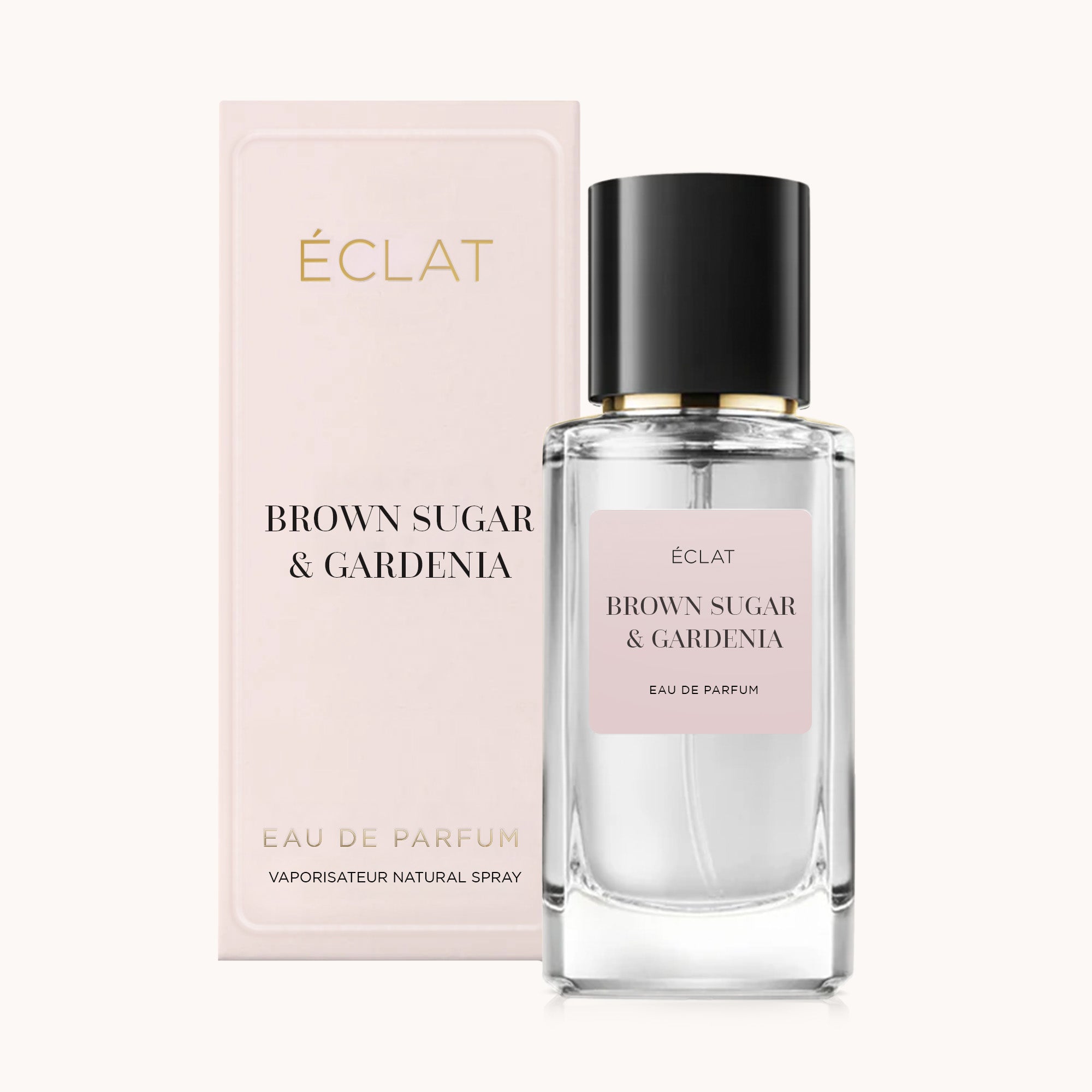 Ein facettierter Glasflakon des Parfums ÉCLAT Brown Sugar & Gardenia mit schwarzer Kappe, neben einer rosafarbenen Präsentbox.