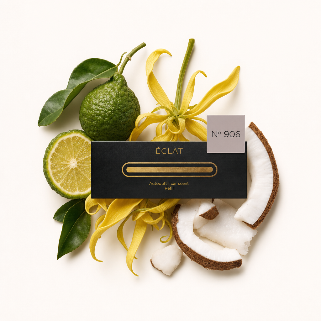 Ein Arrangement aus Bergamotte, Ylang-Ylang-Blüten und Kokosnussstücken umgibt eine schwarze ÉCLAT-Autoduftkappe mit Etikett.
