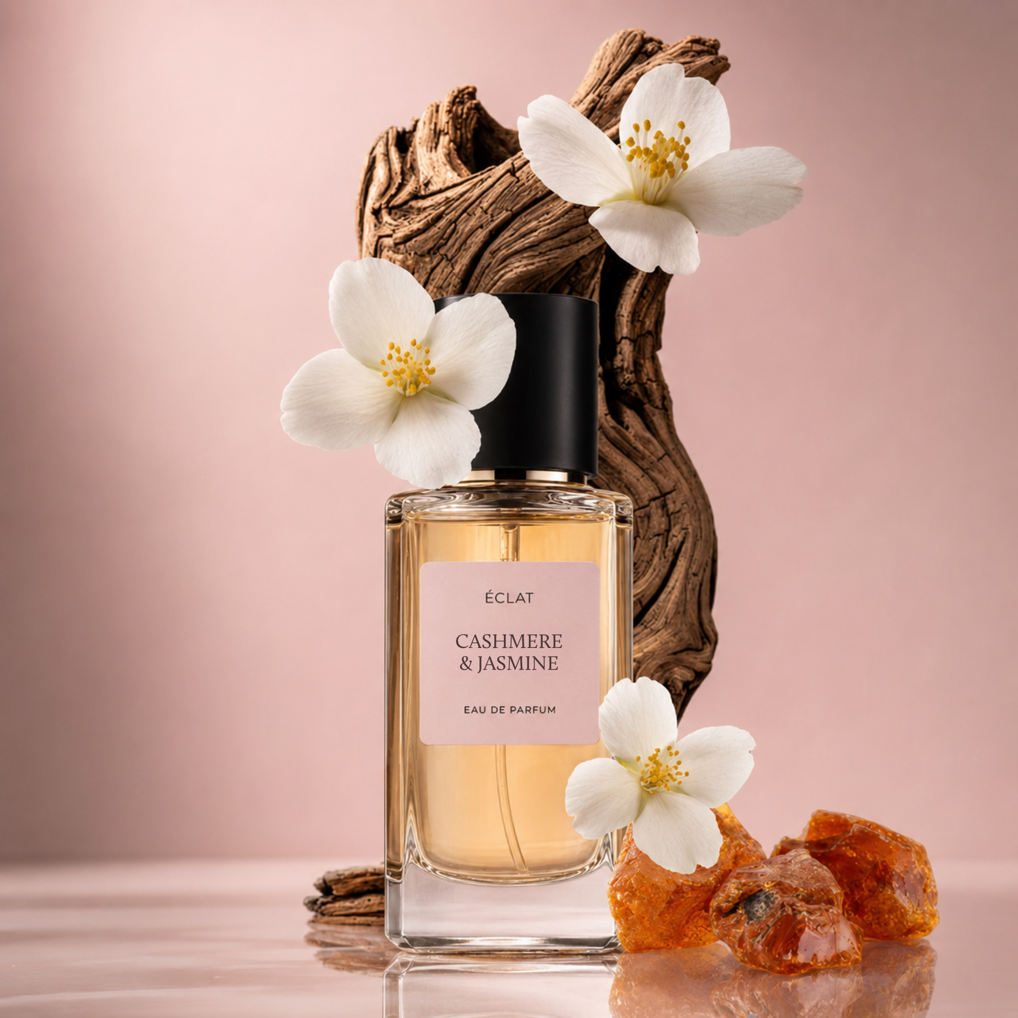 Ein klarer Glasflakon des ÉCLAT Cashmere & Jasmine Parfums mit schwarzem Verschluss, umgeben von weißen Jasminblüten und Bernsteinsteinen auf einem strukturierten Holzuntergrund.