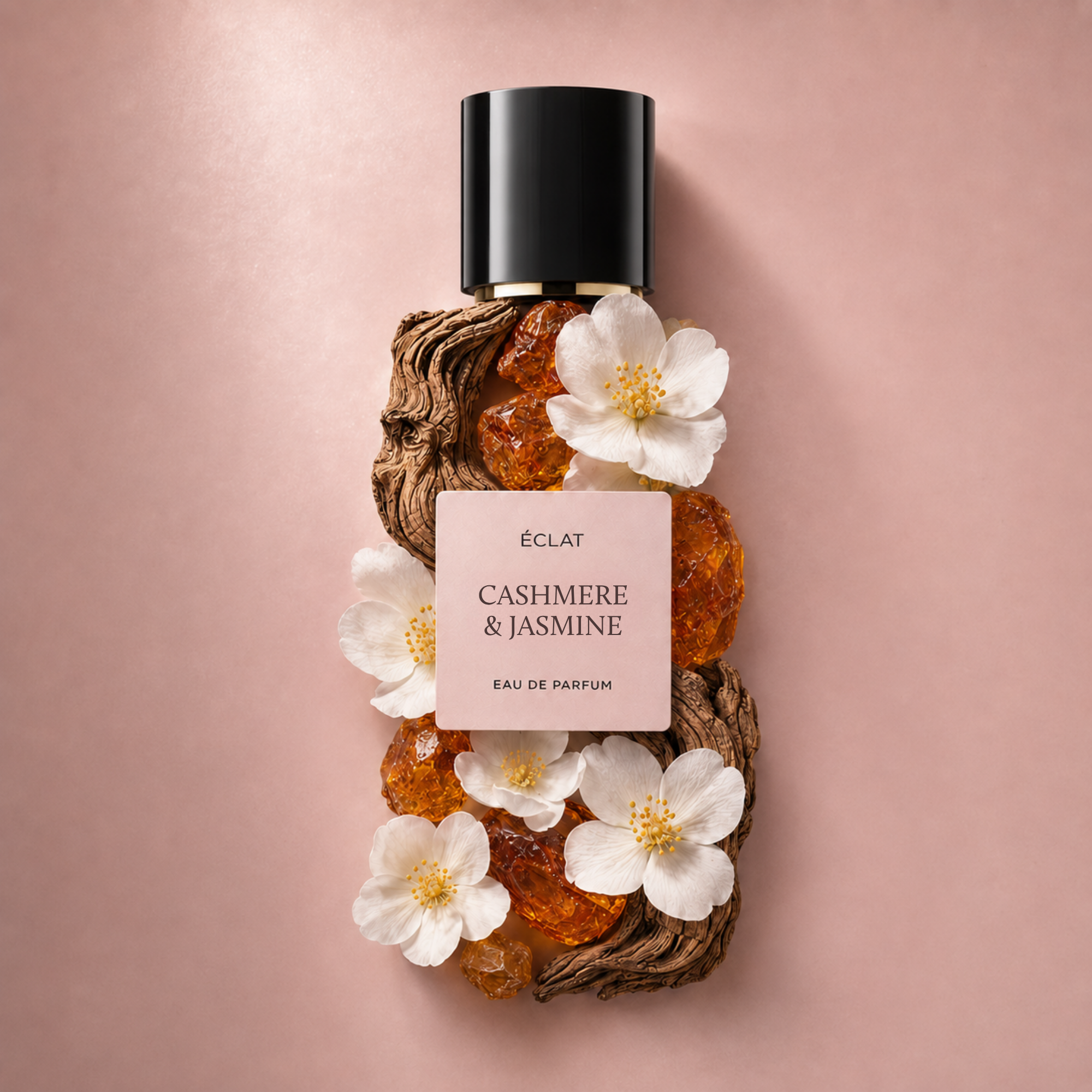 ÉCLAT Cashmere & Jasmine Parfumflakon verziert mit weißen Blüten und Bernsteinkristallen vor einem rosa Hintergrund.