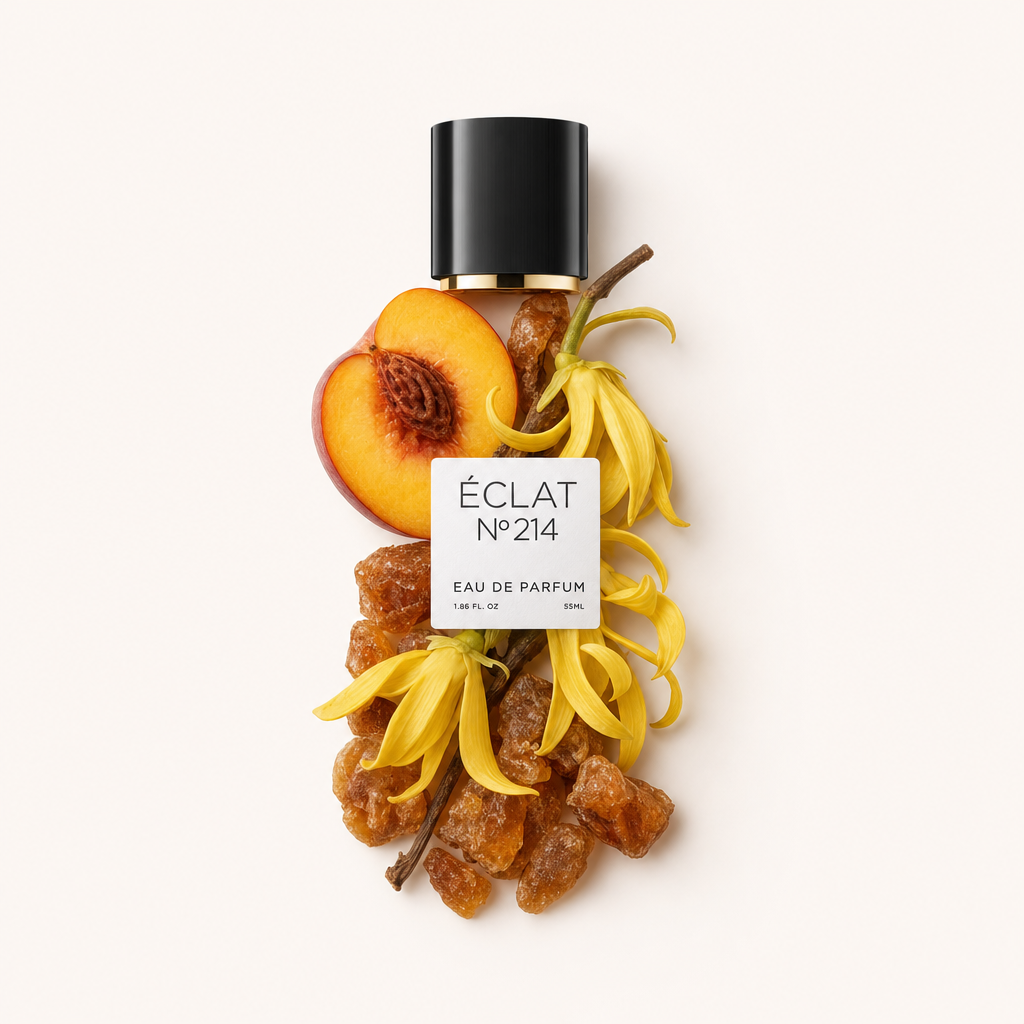 Ein Arrangement aus gelben Ylang-Ylang-Blüten, Amberharz und einer halbierten Pfirsichhälfte umgibt eine schwarze Kappe mit Etikett für ÉCLAT Creamy Amber.