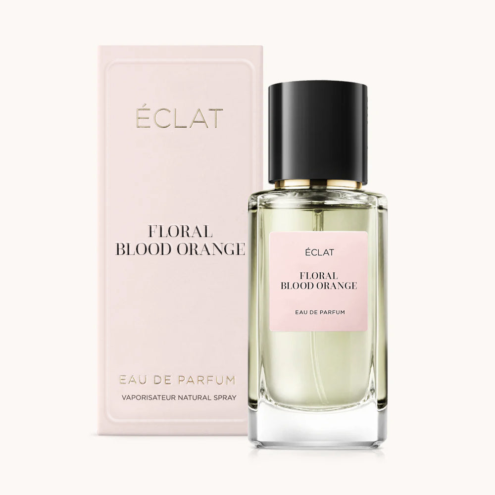 Ein facettierter Glasflakon ÉCLAT Floral Blood Orange mit schwarzem Verschluss neben einer blassrosa Box.