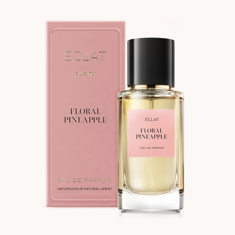 Ein facettierter Glasflakon ÉCLAT Floral Pineapple mit schwarzer Kappe, begleitet von einer rosa Box mit gleichem Namen.