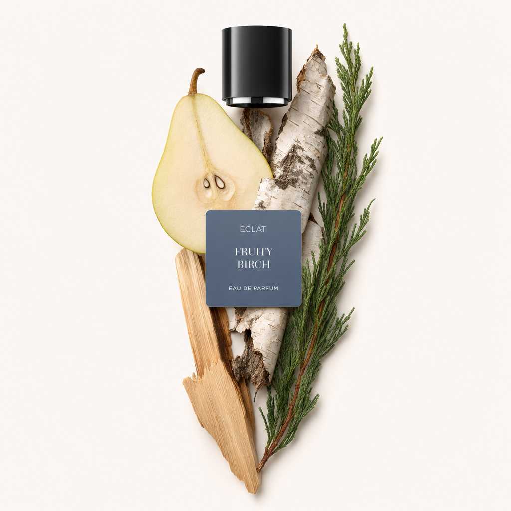Ein kunstvolles Arrangement aus einer aufgeschnittenen Birne, Birkenrinde und Zypressenzweigen, gekrönt von einer schwarzen Kappe mit ÉCLAT Fruity Birch Etikett.