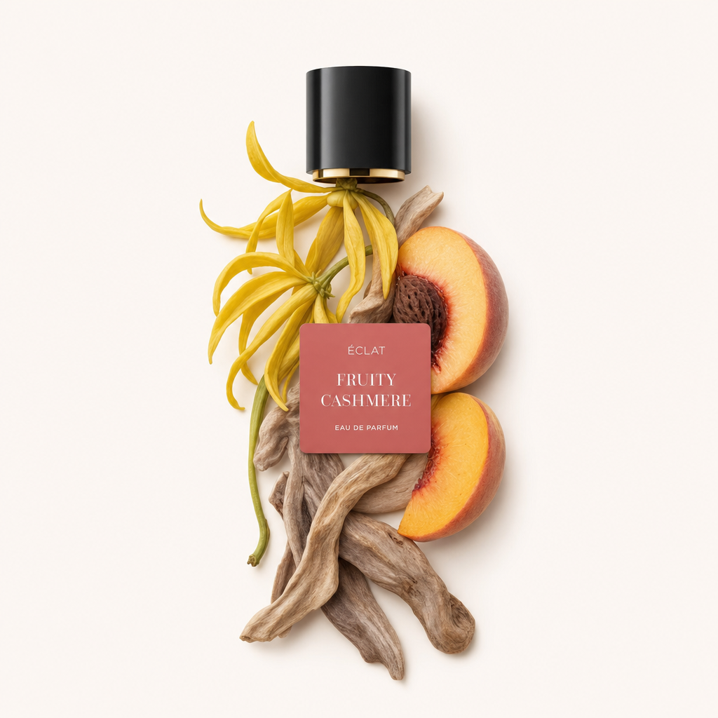 Ein Arrangement aus Ylang-Ylang-Blüten, Pfirsichhälften und Sandelholzstöcken mit einer schwarzen Kappe und einem ÉCLAT Fruity Cashmere Etikett.