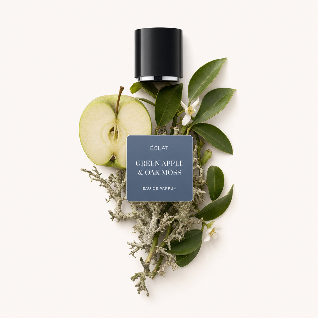 Ein Arrangement aus einer grünen Apfelhälfte, Eichenmoos und üppigen grünen Blättern liegt unter einer schwarzen Kappe mit einem Etikett mit ÉCLAT Green Apple & Oak Moss.