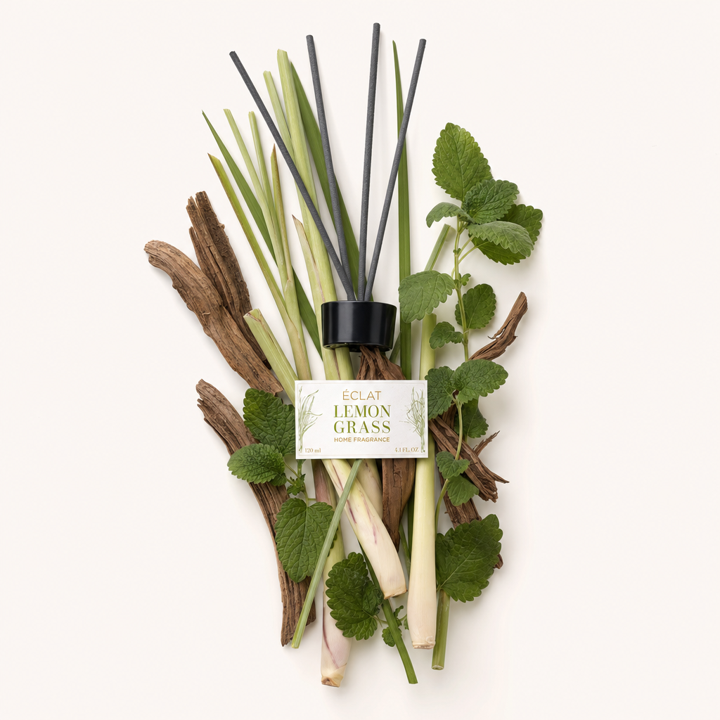 Ein Arrangement aus Zitronengras, Minzblättern und Holzstücken umgibt die schwarze Kappe mit ÉCLAT Lemongrass Room Fragrance Sticks Etikett.