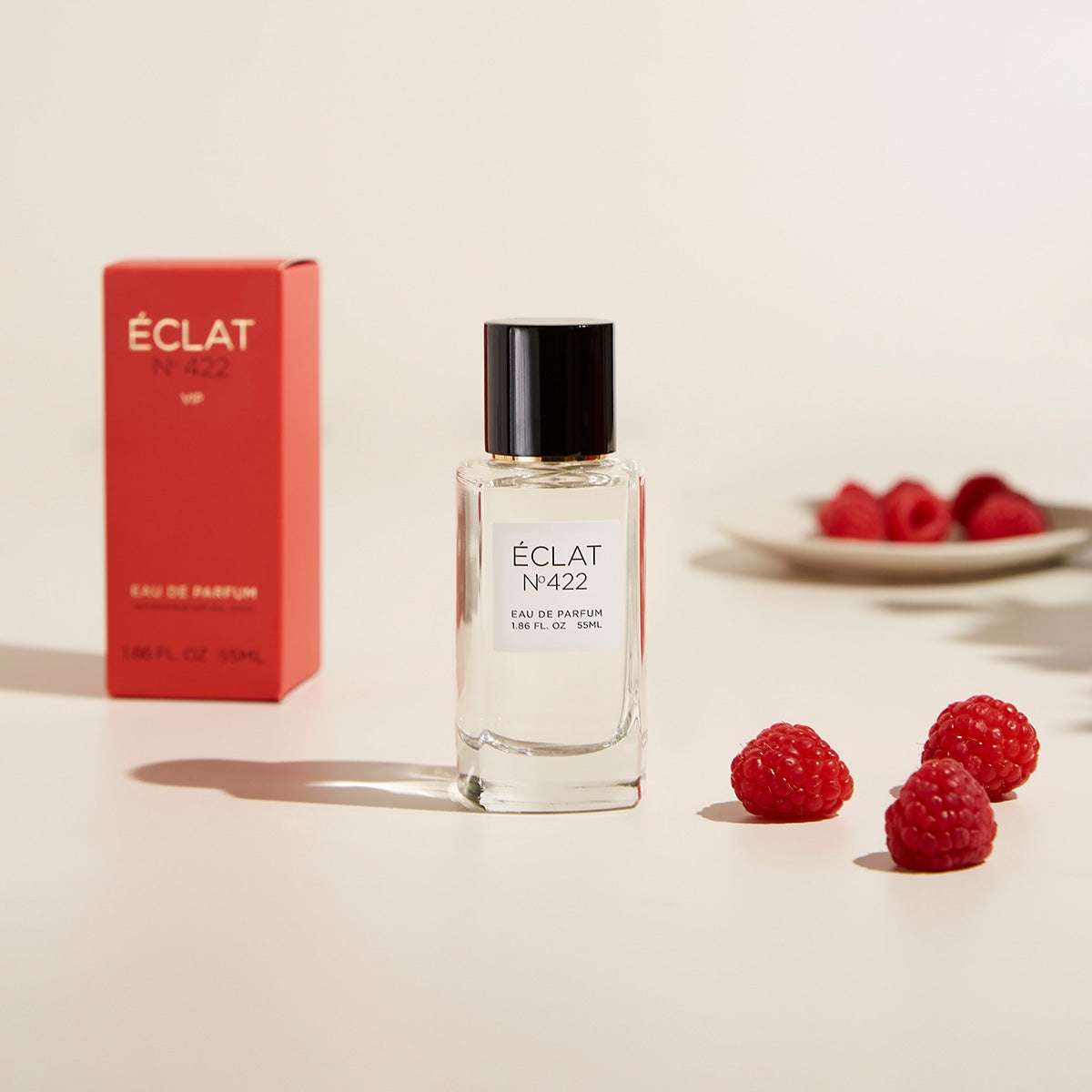 Klarer Glasflakon von ÉCLAT Musky Passionfruit mit schwarzer Kappe, begleitet von einer roten Verpackungsbox und frischen Himbeeren.