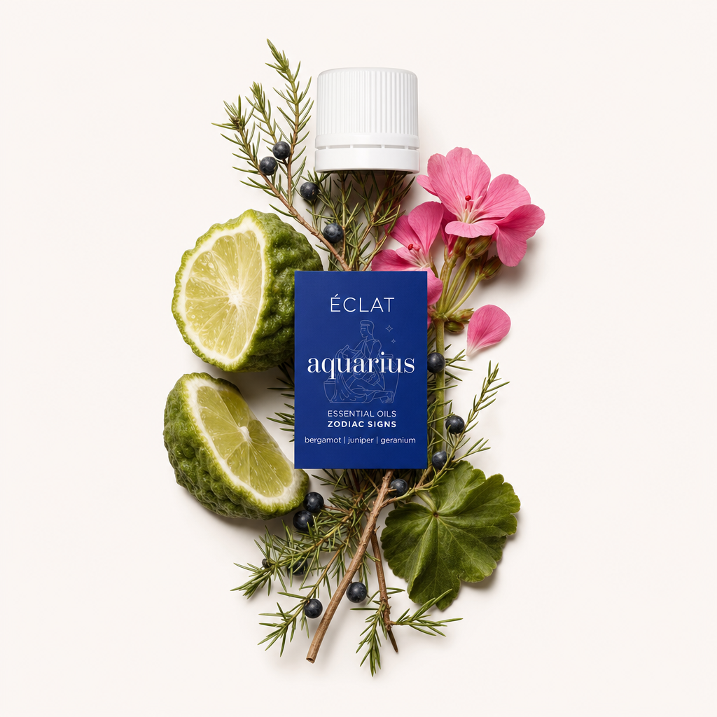 Ein Arrangement aus Bergamottenscheiben, Wacholderzweigen mit Beeren und rosa Geranienblüten umgibt eine schwarze Kappe mit Etikett des ÉCLAT-Zodiac Sign Aquarius-Öls.