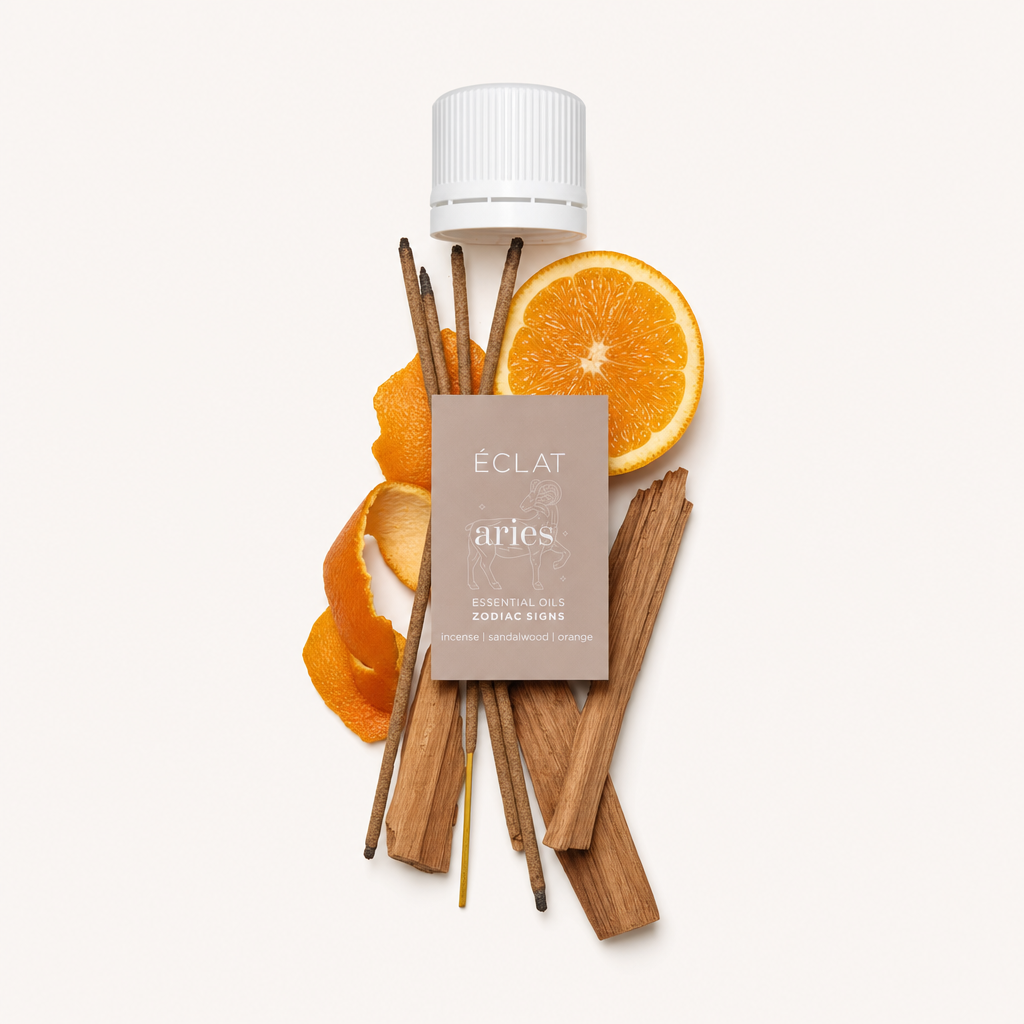 Ein Arrangement aus rohen Räucherstäbchen, Sandelholzstücken und einer geschnittenen Orange, oben eine schwarze Kappe mit einem Etikett für ÉCLATs Widder-Öl.
