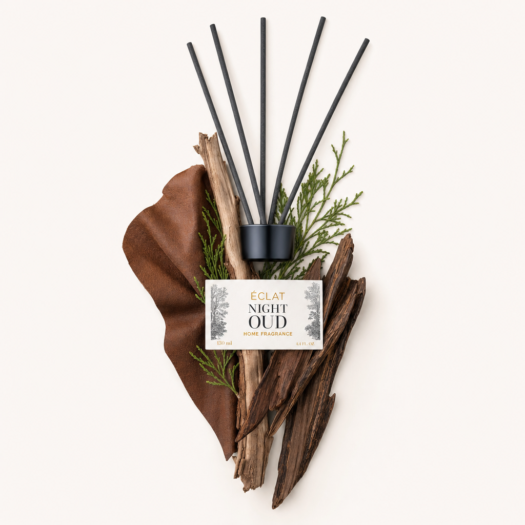 Ein Arrangement aus ÉCLAT Night Oud Duftzutaten wie trockenem Holz, grünen Zweigen und einem ledrigen Element, gekrönt von einer schwarzen Kappe mit Etikett.