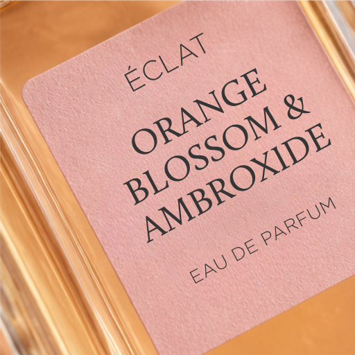 Ein facettierter Glasflakon mit einem rosa Etikett, das den Namen ÉCLAT Orange Blossom & Ambroxide zeigt.