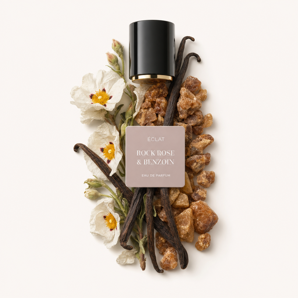 Ein Arrangement aus Vanilleschoten, Zistrosenblüten und Benzoeharz umgibt eine schwarze Kappe mit goldenem Rand und dem Etikett ÉCLAT Rock Rose & Benzoin.