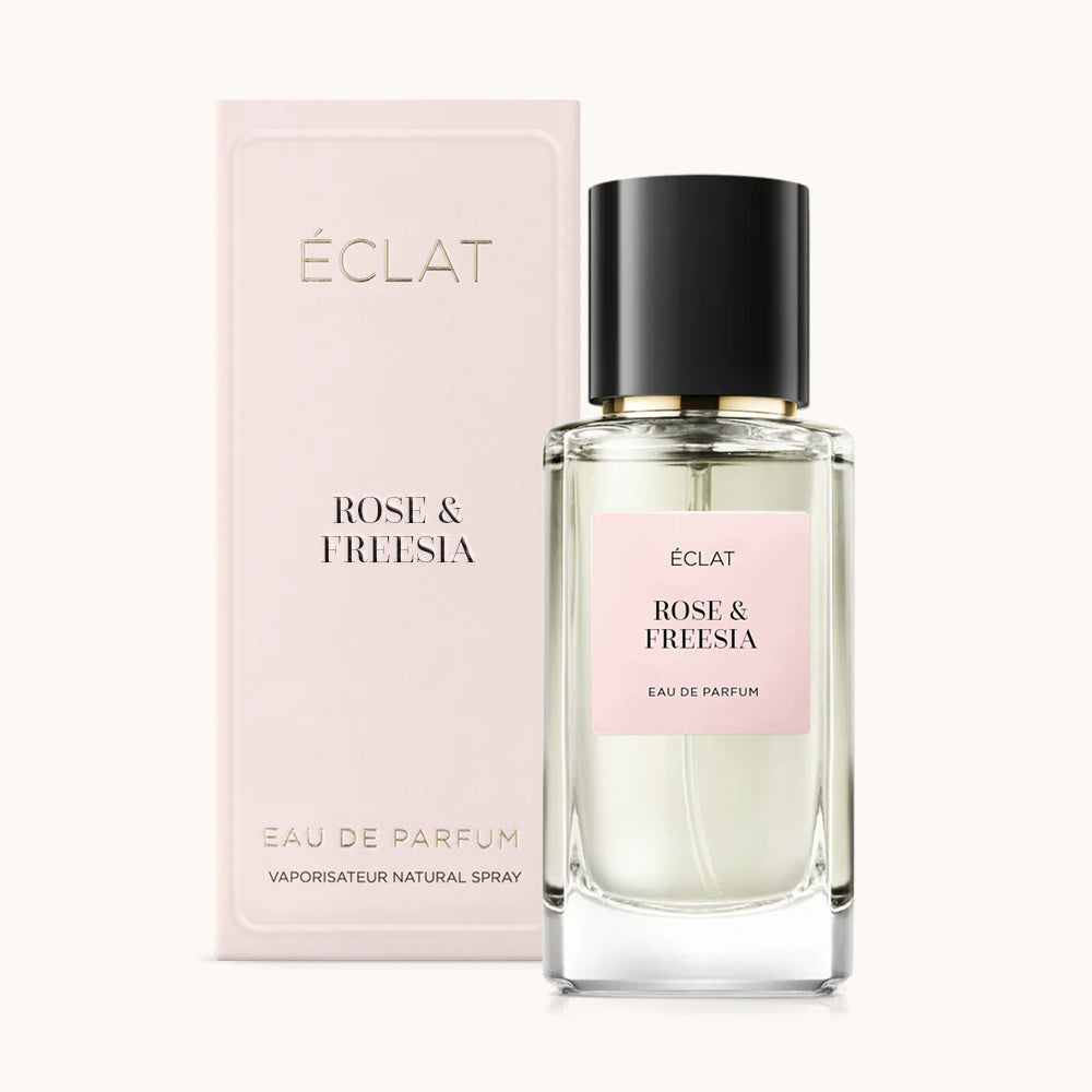 Ein facettierter Glasflakon mit mattem rosa Etikett für ÉCLAT Rose & Freesia, begleitet von einer passenden rosa Box im Hintergrund.