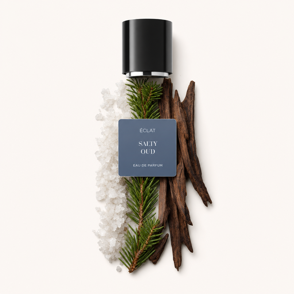 Ein Arrangement aus groben Salzkristallen, immergrünen Zweigen und dunklen Holzstücken neben einer schwarzen Kappe mit ÉCLAT Salty Oud Etikett.