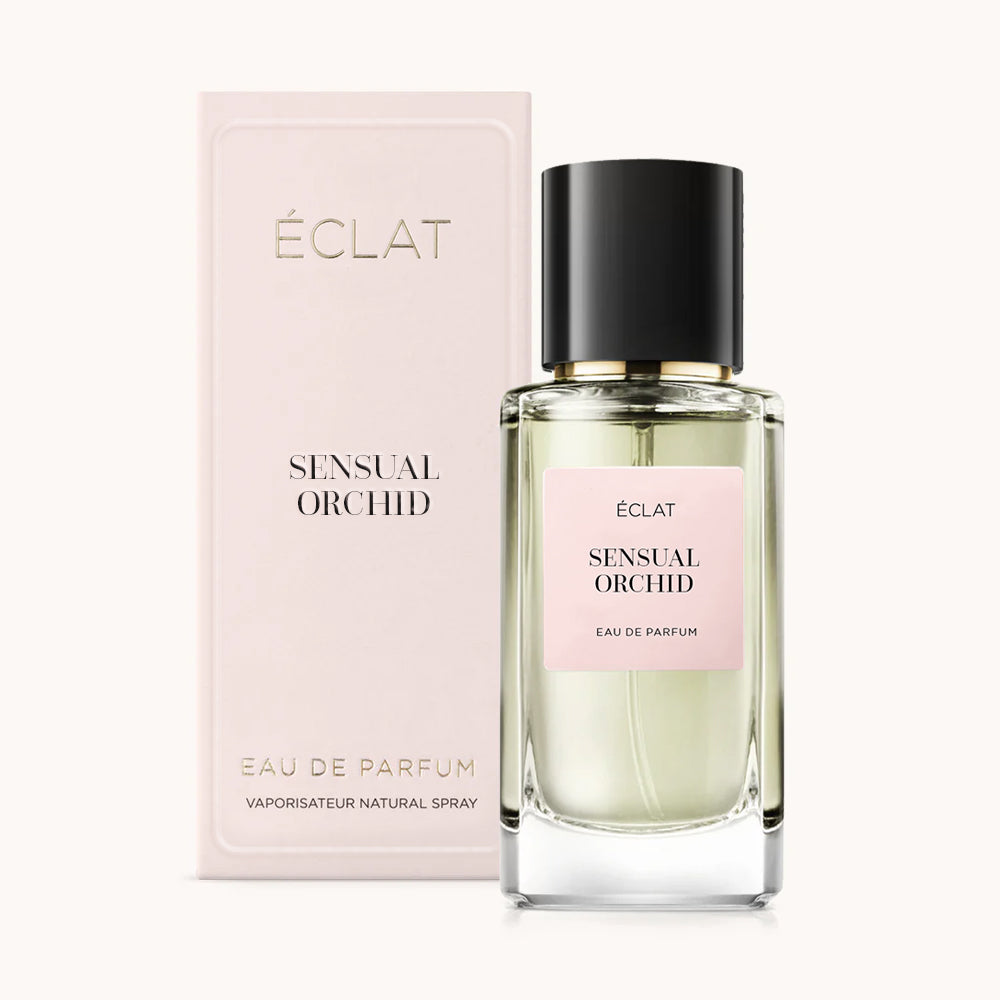 Ein facettierter Glasflakon mit schwarzem Verschluss und rosa Etikett steht neben seiner passenden rosa Präsentbox für ÉCLAT Sensual Orchid.