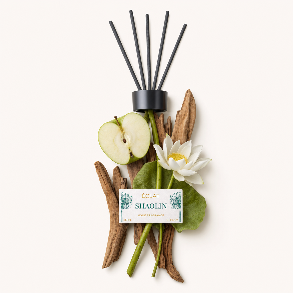 Ein Arrangement aus Holzstöcken, einem halbierten grünen Apfel, einer weißen Lotusblume und Blättern ist kunstvoll um die schwarze Kappe mit dem Etikett der ÉCLAT Shaolin Raumduftstäbchen drapiert.