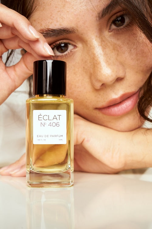 Ein facettierter Glasflakon von ÉCLAT N° 406 Eau de Parfum mit schwarzer Kappe vor dem Gesicht einer Person.