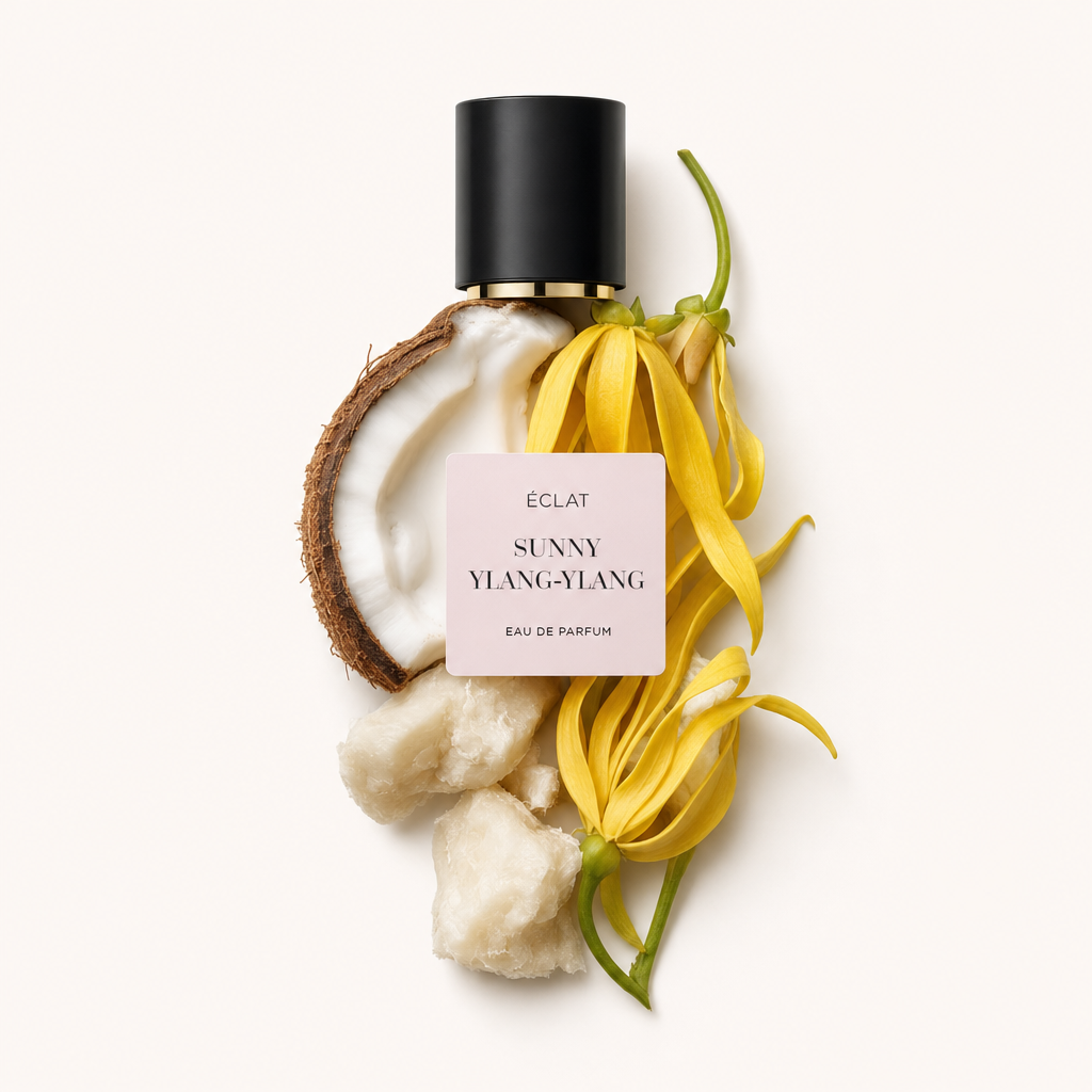 Ein Arrangement aus frischen Ylang-Ylang-Blüten, halber Kokosnuss und Stücken von Sheabutter, mit einer schwarzen Kappe mit ÉCLAT Sunny Ylang-Ylang Etikett.