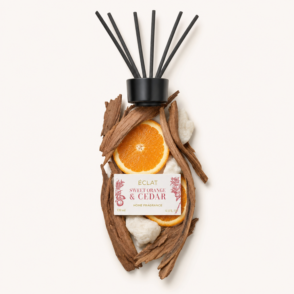 Ein Arrangement aus Zedernholzstücken und süßen Orangenscheiben umschließt eine schwarze Kappe mit dem Etikett von ÉCLAT Sweet Orange & Cedar Raumduftstäbchen.