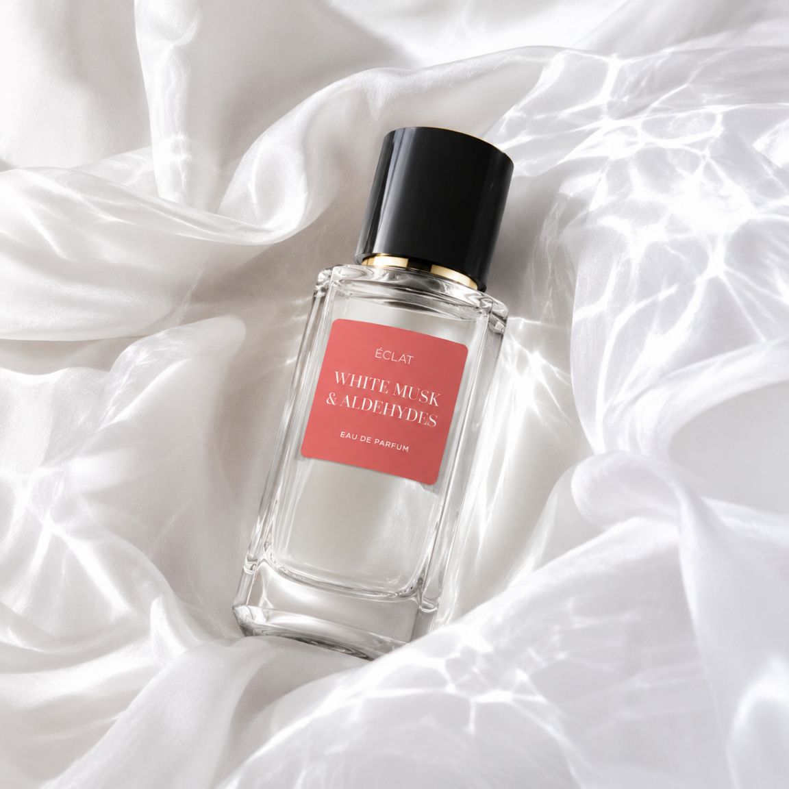 Ein facettierter Glasflakon von ÉCLAT White Musk & Aldehydes mit schwarzer Kappe und korallenfarbenem Etikett liegt auf einem Satin-Hintergrund.