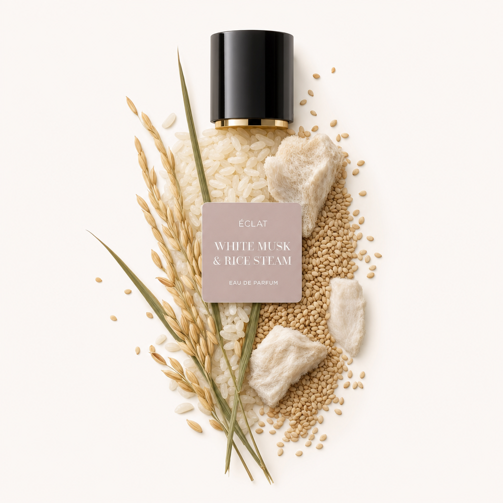 Ein kunstvolles Arrangement aus Reiskörnern, flauschigen Moschusstücken und Getreidekörnern umgibt eine schwarze Kappe mit einem Etikett, das ÉCLAT White Musk & Rice Steam zeigt.