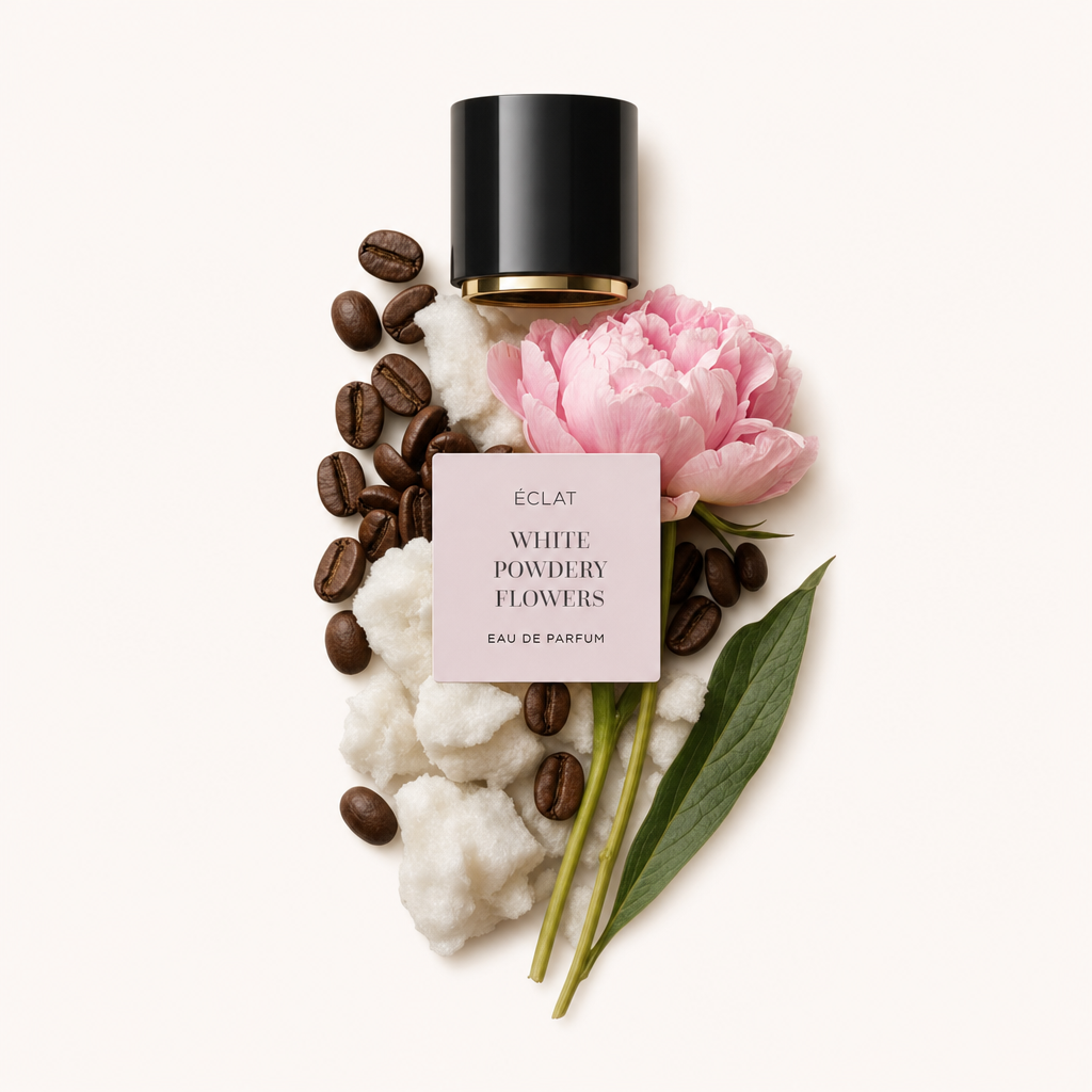 Ein Arrangement aus Watte, Kaffeebohnen und einer rosa Pfingstrose neben einer schwarzen Kappe mit einem Etikett, das ÉCLAT White Powdery Flowers zeigt.