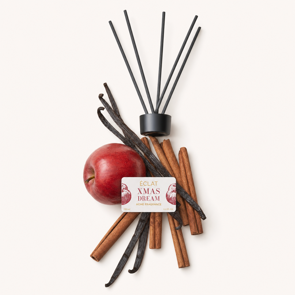 Ein Arrangement aus einem roten Apfel, Zimtstangen und Vanilleschoten für ÉCLAT Xmas Dream Raumduft-Stäbchen neben der originalen schwarzen Verschlusskappe mit Etikett.